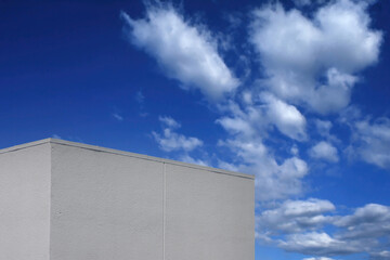 Wall Mural - Top of a white windowless building and blue sky with clouds