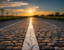 Straight Road With An Arrow Painted On It, Leading Towards The Horizon The Sun Is Setting In The Background Casting Long Shadows Over Cobblestones And Asphalt