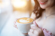 Close up holding Hot coffee latte with latte art milk foam in cup mug with happy Smiling woman relaxing sitting in cafe interior in coffee shop background,Business Lifestyle summer holiday concept