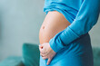 Close-up of young pregnant woman touching her belly and caring about her health. Motherhood and baby expectation concept