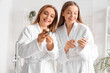 © Pixel-Shot - Young woman and her mother with jar of cream using mobile phone after shower in bathroom