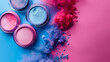 A creative display of makeup with open containers of crushed blue and pink eyeshadow beside swirls of soft pink fabric on a gradient background..
