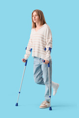 Poster - Injured young woman after accident with crutches on blue background