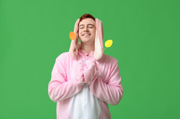 Poster - Happy young man in Easter bunny costume with paper eggs on green background