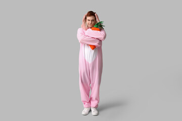 Poster - Thoughtful young man in Easter bunny costume holding plush carrot on white background