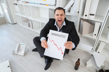 Wall Mural - Drunk businessman holding paper with word BANKRUPTCY in office