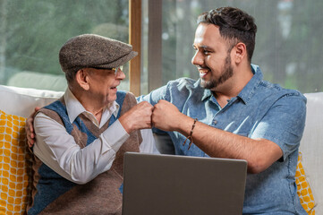 Happy adult senior father with his adult son. Young man enjoys teaching his older father how to use a laptop. How to use technology.