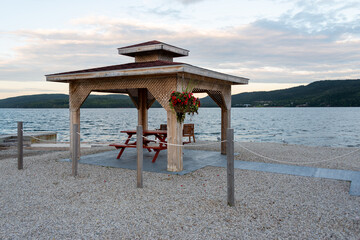 A large four-sided wooden gazebo overlooking the Bay of Fundy.  The roof is covered in green metal panels. There's a green picnic table under the arbor. The river is low with red mud on both sides.