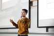 © fotolite - Student giving a presentation speech in front of a projector screen in a room