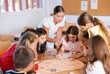 © JackF - Happy preteen children and female teacher playing together educational board game in classroom at elementary school