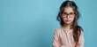 Against a light blue backdrop, a young girl strikes a confident stance, her glasses framing her face as she gazes directly at the camera with a determined expression