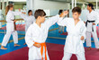 © JackF - Boys and girls in karate uniform training combat moves in gym. Trainer standing nearby and watching.