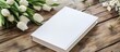 A book with a white cover is placed on a tabletop, surrounded by a bunch of vibrant flowers
