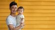 An elated Chinese father in a white T-shirt holding a baby with gentle care