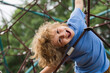 The outdoor playground for children in summer park. Kid play on playground under the tree. Portrait of excited blonde kid doing rock climbing with greenery in the background.