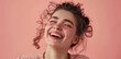 Close-up of a cheerful young woman laughing heartily against a pink background