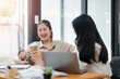 © Satori Studio - Two joyful women sharing a light-hearted moment with coffee in hand, working together at an office desk.