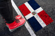 a woman with a boots standing on asphalt next to flag of Dominican Republic and border
