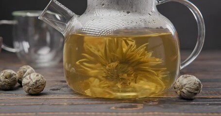 Wall Mural - Blooming flower tea ball brewing in a glass teapot with Hot boiling water on wooden background