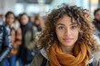 © Good Shot - A young woman with curly hair stands poised in a bustling city street, with people blurred in motion around her.