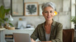 © boxstock production - Happy business woman wearing olive business casual shirt sitting at table with laptop looking at camera with positive smile in modern startup office