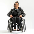A smiling young woman with glasses, dressed in winter clothes, sitting in a wheelchair on a white background.