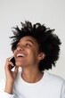 Happy young African American woman talking on the phone, showing genuine laughter and delight on a clean background.