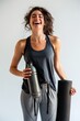 A laughing woman holding a water bottle and yoga mat, radiating post-workout happiness and health.