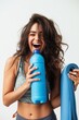 A beaming young woman holding a yoga mat and blue water bottle, embodying vitality and happiness post-workout.