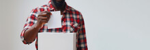A Man Is Holding A Piece Of Paper In It. He Is Wearing A Red And White Plaid Shirt. African American Male Hand Putting Vote In Ballot Box. Ballot Box With Man Casting Vote On White Blank Voting Slip