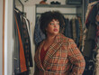 © Moritz - Body Positive Concept: Plus Size Woman Choosing Clothes in Home Wardrobe. Overweight Young Woman Holding Hangers with Blouses, Contemplating Fashion Choices in Front of Mirror