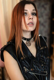 Fototapeta  - Beautiful curvy woman in a leather vest with spikes in punk style in an old apartment posing
