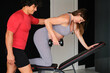 Pregnant woman working out with a dumbbell supervised by a male personal trainer at the gym.