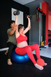Pregnant woman exercising with dumbbells and fitball with personal trainer's help at the gym.