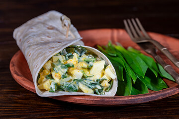 Wall Mural - Homemade burrito wraps with boiled eggs, potato, green wild garlic and sour cream for healthy breakfast on plate, closeup