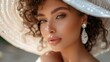 Elegant bride wearing a white summer hat, showcasing wedding makeup and a curly hairstyle. The fashion model's face is captured in a portrait, highlighting crystal earring jewelry.