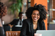 © AI_images - A cheerful woman in business attire smiles happily while seated in the office boardroom, her laptop open in front of her.