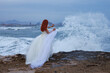 Mujer pelirroja con vestido de novia en la playa y salpicaduras de ola de mar con gesto de parar el splash, Alicante, España