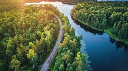 Aerial view of country road in green summer forest with blue lakes at sunset in Finland