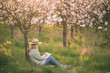 Relaxed woman is writing her diary and resting in blooming cherry orchard. Joy the moment in spring nature