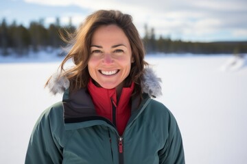Portrait of a grinning woman in her 40s wearing a functional windbreaker in backdrop of a frozen winter lake