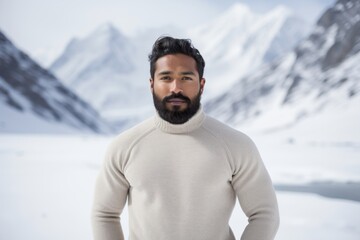 Wall Mural - Portrait of a glad indian man in his 20s showing off a thermal merino wool top isolated in pristine snowy mountain