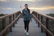 © Cristian Blázquez - Young woman checking her phone on a wooden boardwalk at dusk
