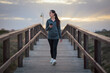 © Cristian Blázquez - Young woman checking her phone on a wooden boardwalk at dusk