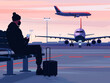 A traveler with luggage waiting at an airport terminal, looking at the phone with airplanes in the background at sunset.