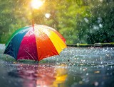 Fototapeta Tęcza - Multicolored rainbow umbrella on the ground catches raindrops against blurred nature backdrop