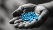 A black and white toned photo shows a blue pill in an open palm