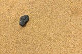 Fototapeta Przestrzenne - single black stone in a fine sand at the beach