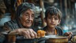 Elderly woman and grandson sharing a meal in a humble setting. World Refugee Day