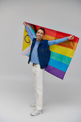 positive appealing gay man in vibrant casual attire holding rainbow flag and smiling at camera